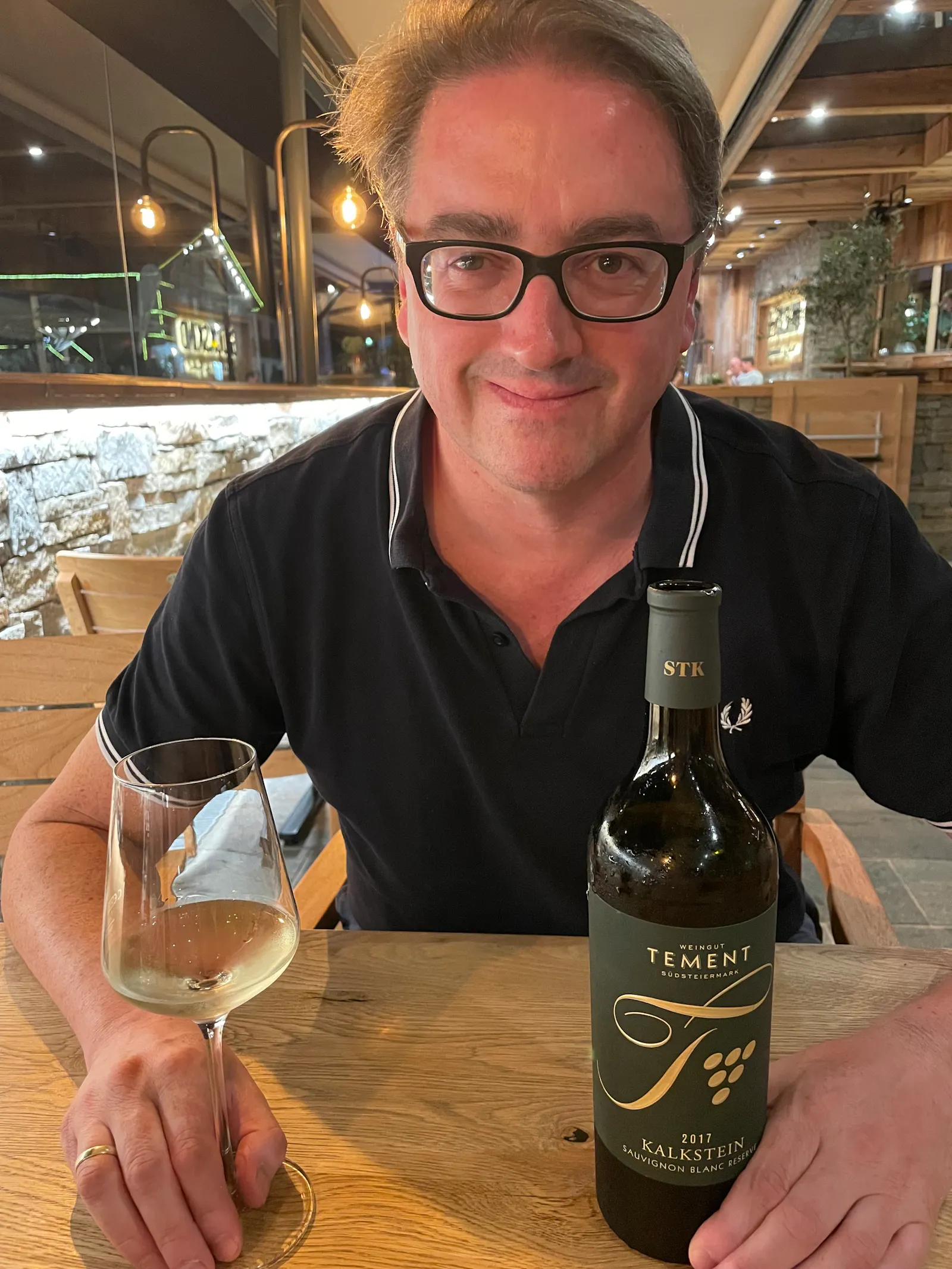 Mann sitzt im Restaurant vor einer Flasche und einem Glas Weißwein.