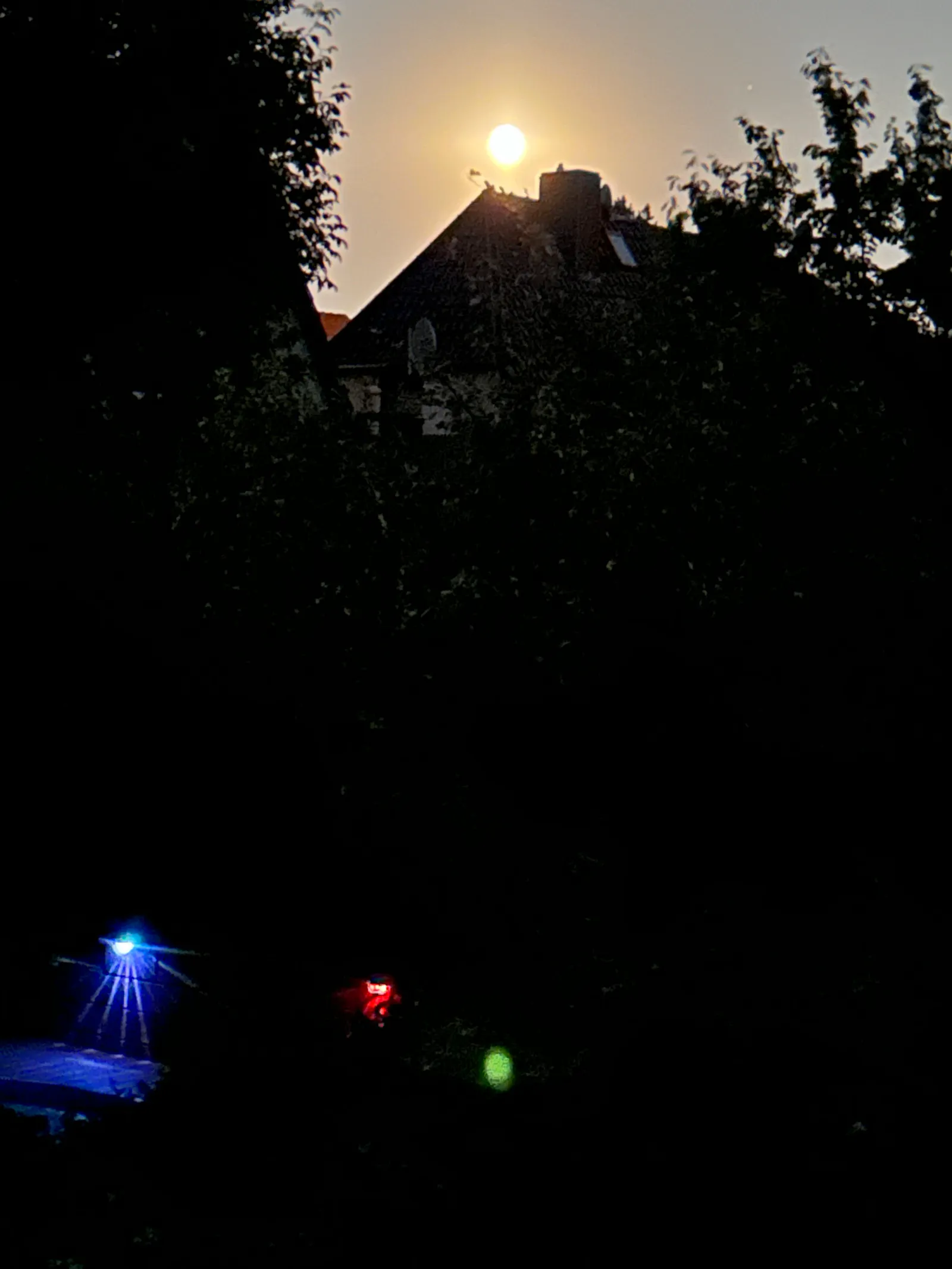 Vollmond über Haus, bunten Leuchten am unteren Bildrand