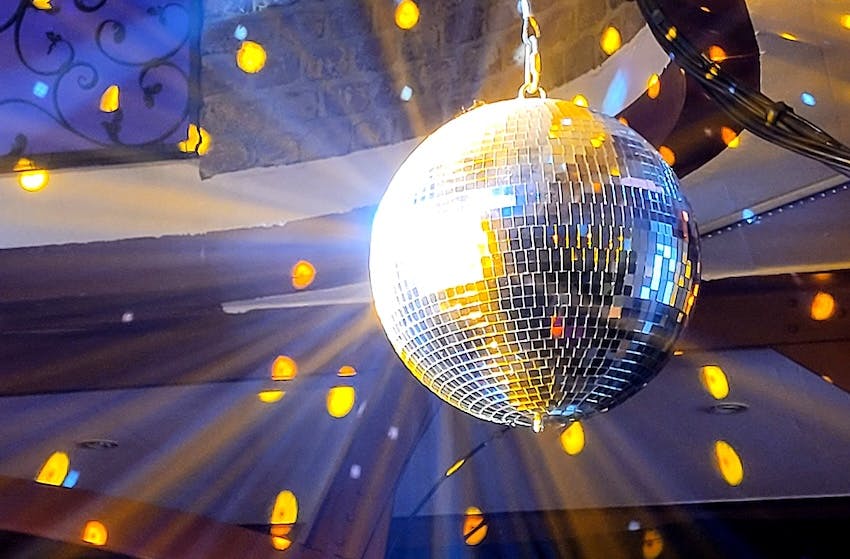Eine Discokugel im Scheinwerferlicht, die gelbe Lichtpunkte an die umliegenden Wände wirft