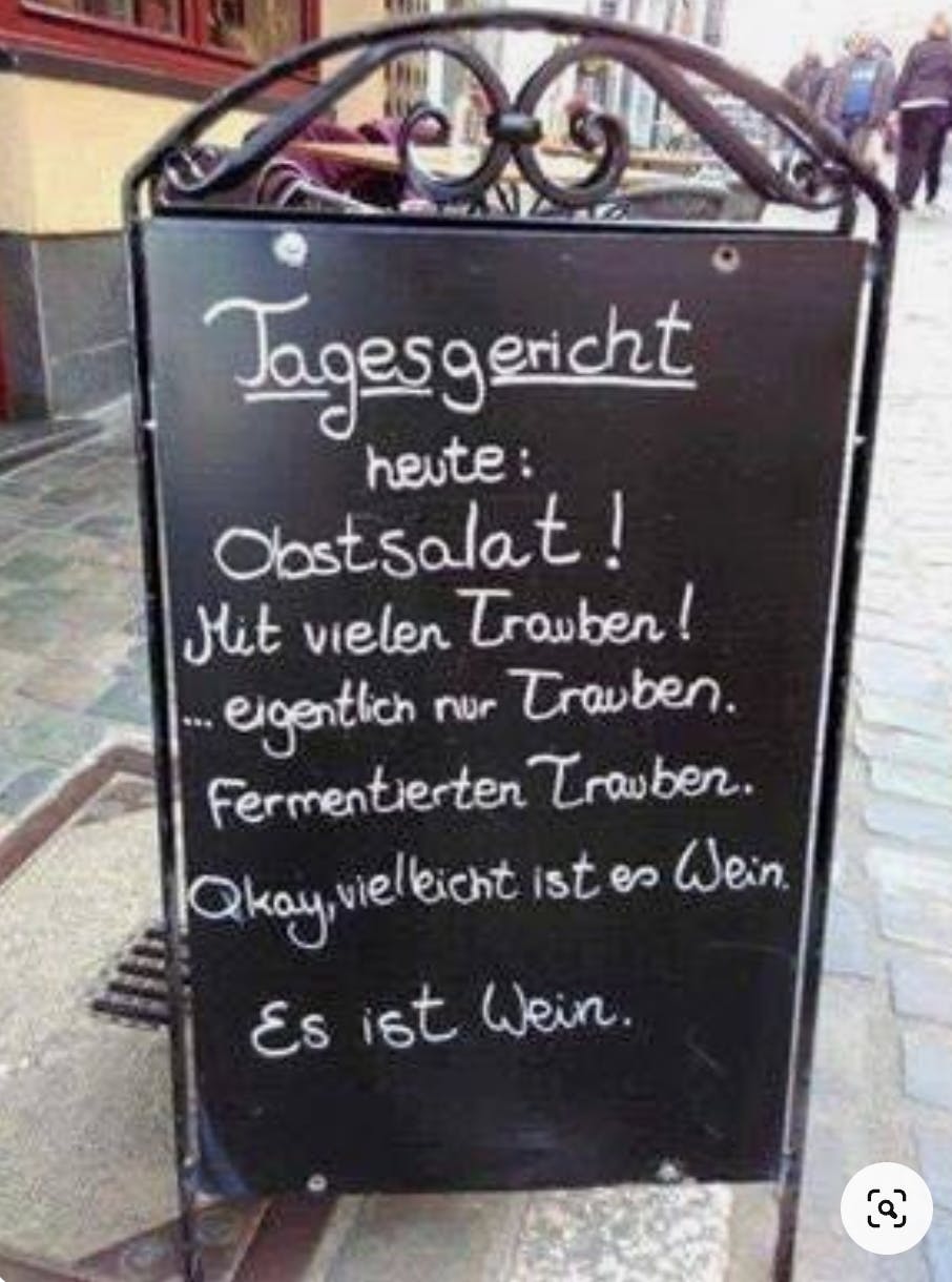Schild: »Tagesgericht heute: Obstsalat! Mit vielen Trauben! ... eigentlich nur Trauben. Fermentierten Trauben. Okay, vielleicht ist es Wein. Es ist Wein.«