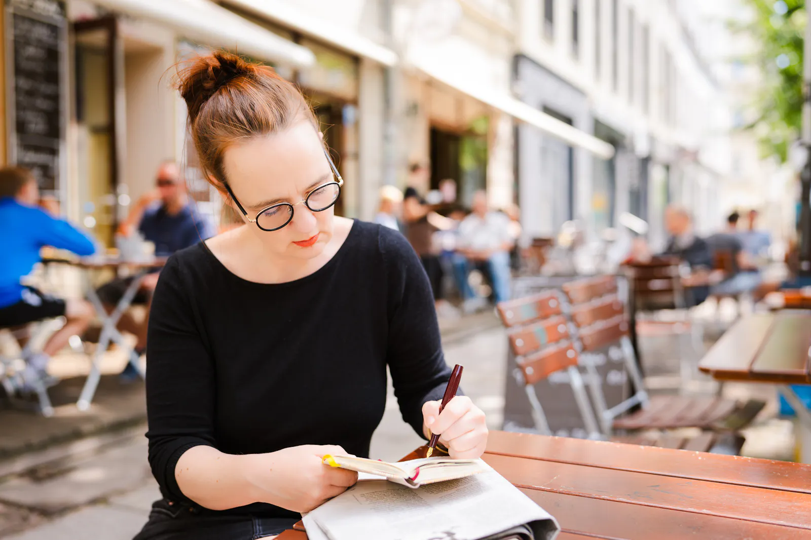 Insa van den Berg, Frau mit roten Haaren und Brille, sitzt an einem Tisch und macht sich mit einem Füller Notizen in einem Heft.