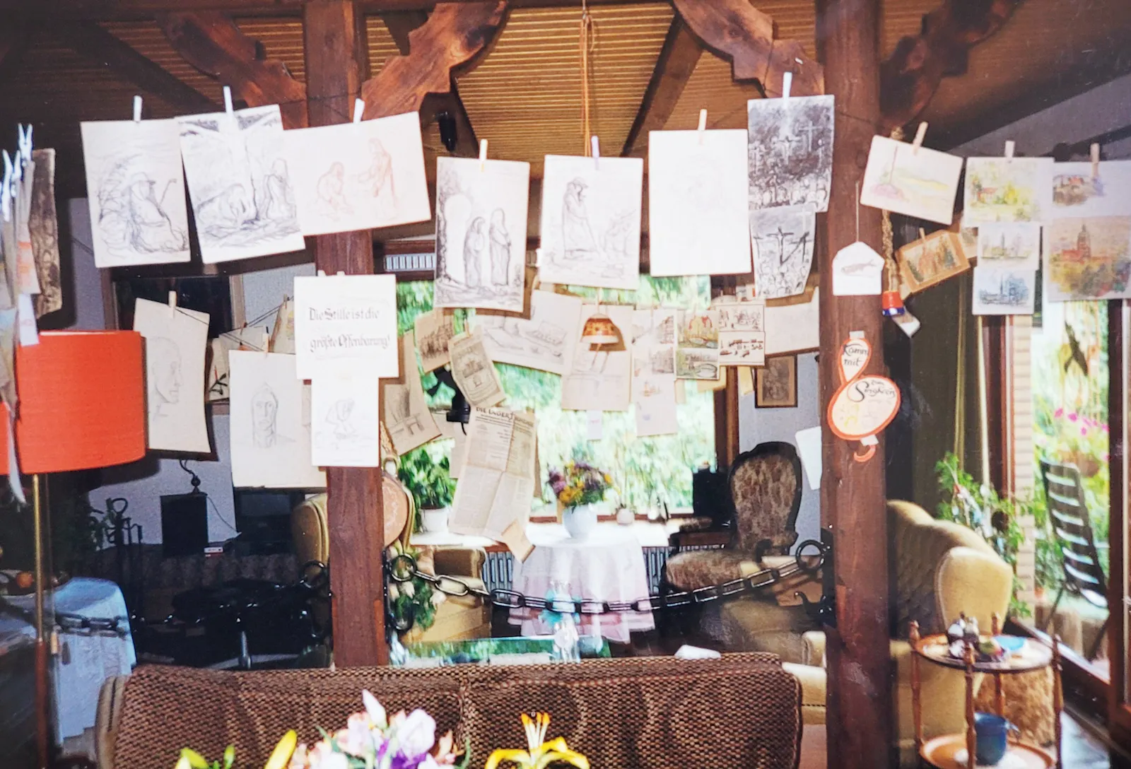 Zeichnungen und Aquarelle hängen an Wäscheleinen in einem Wohnzimmer.