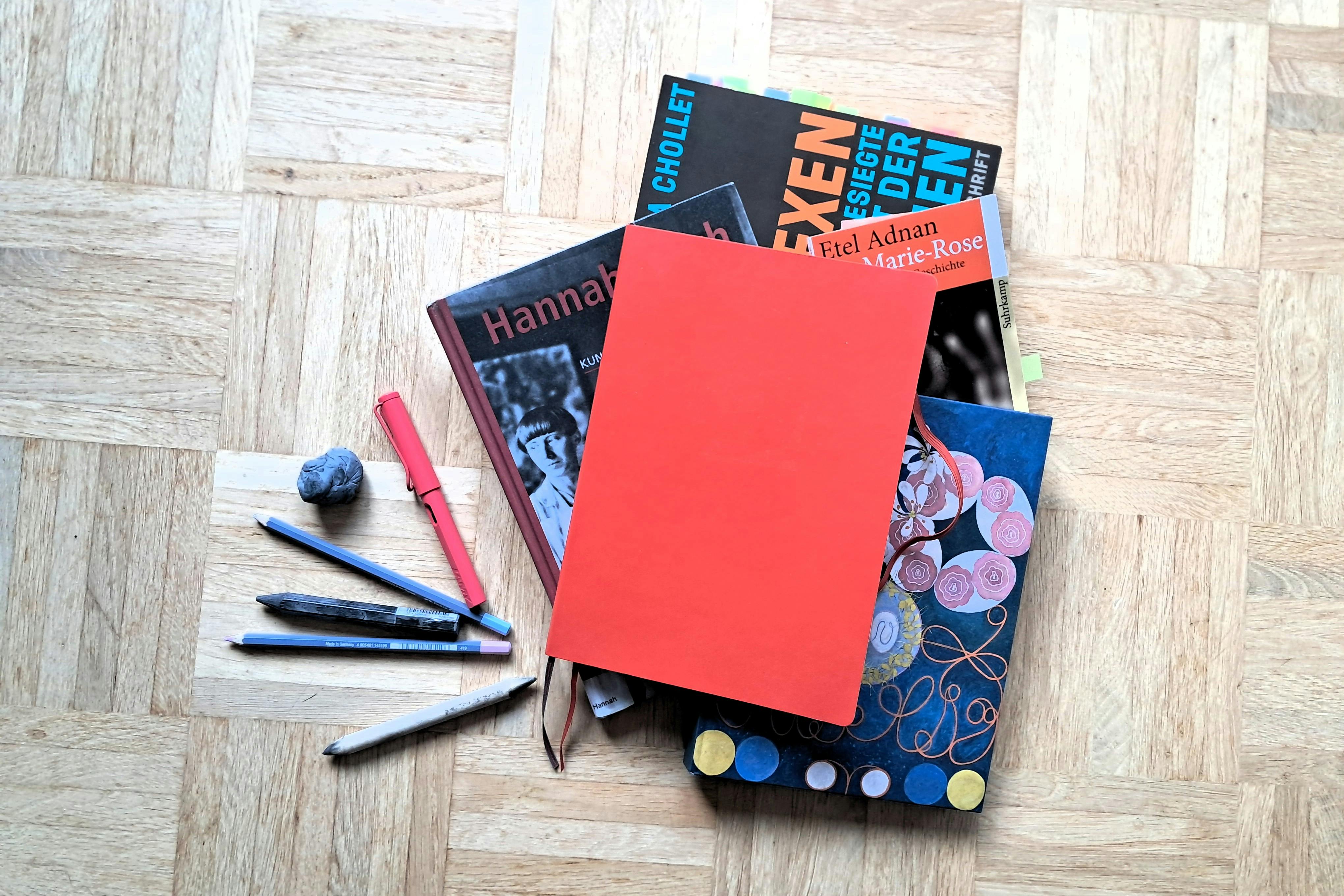 Verschiedene Bücher, Stifte und Notizbücher liegen auf dem Boden.