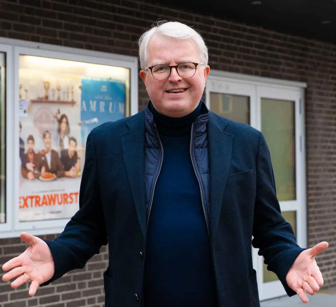 Frank Schäffler vor einem kommunalen Kino, im Hintergrund wird der Film "Extrawurst" beworben