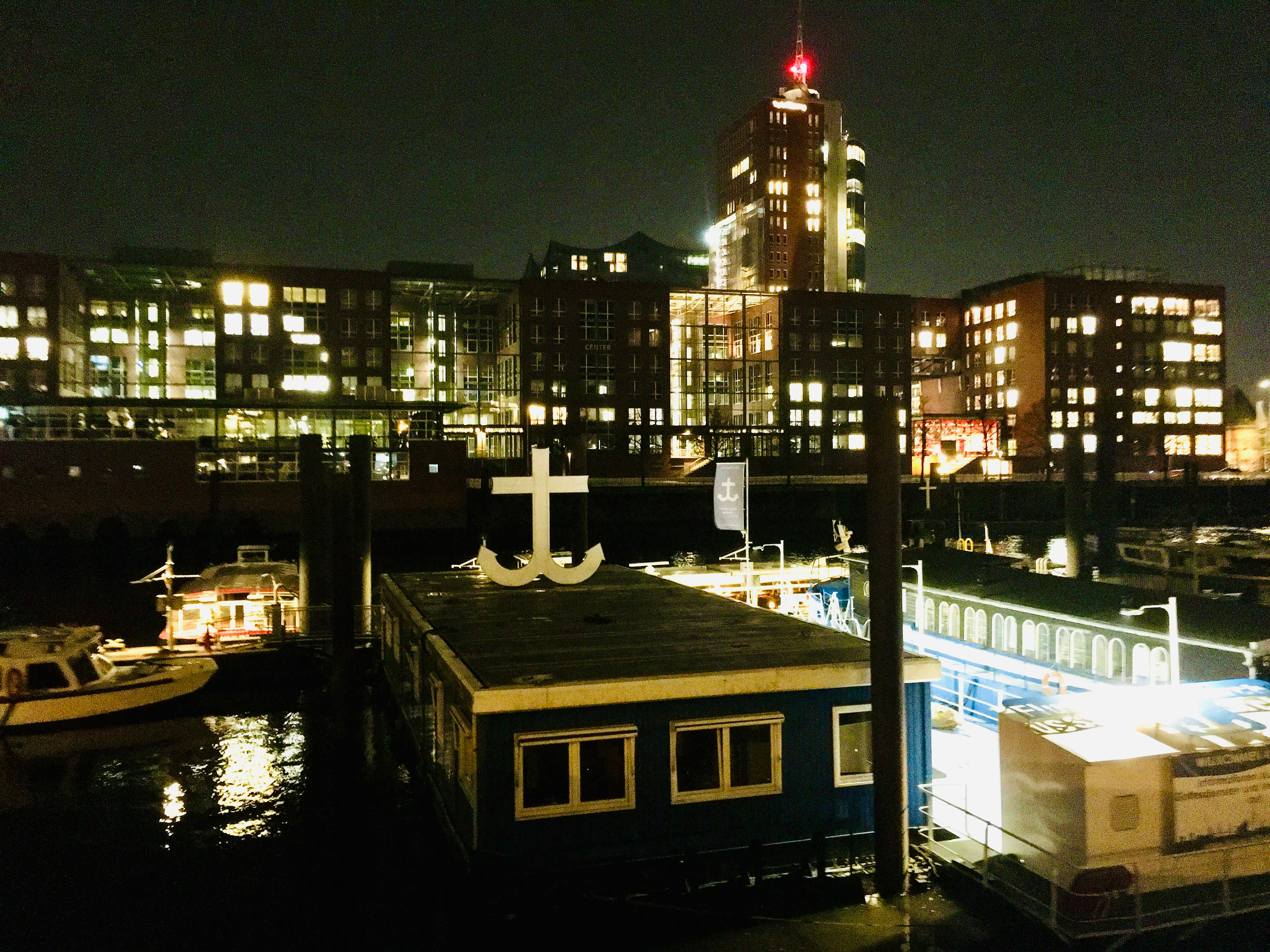 Viele Häuser mit beleuchteten Fenstern, davor die Flussschifferkirche mit einem Symbol auf dem Dach, das einer Mischung aus Kreuz und Anker gleicht.