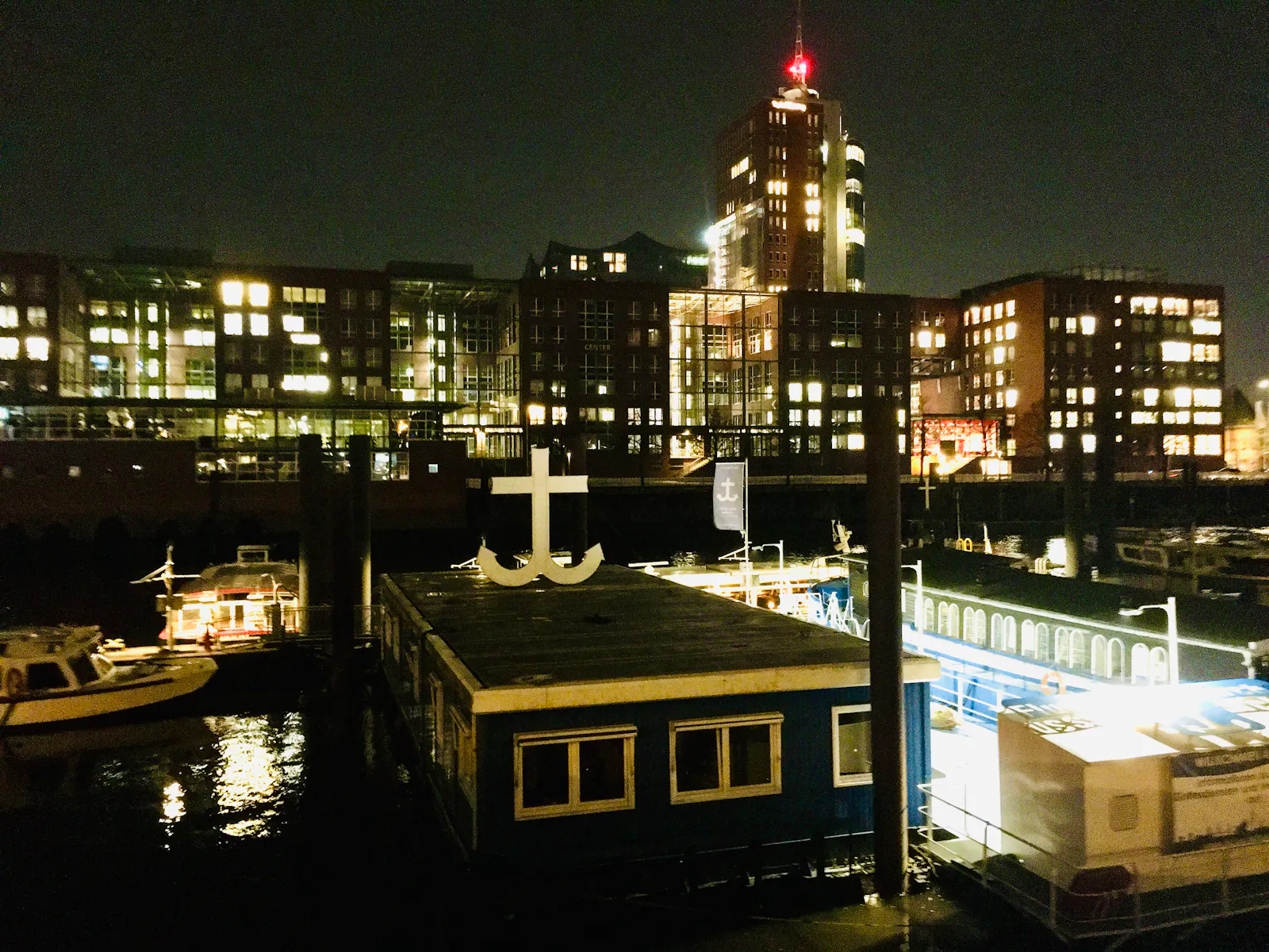Viele Häuser mit beleuchteten Fenstern, davor die Flussschifferkirche mit einem Symbol auf dem Dach, das einer Mischung aus Kreuz und Anker gleicht.