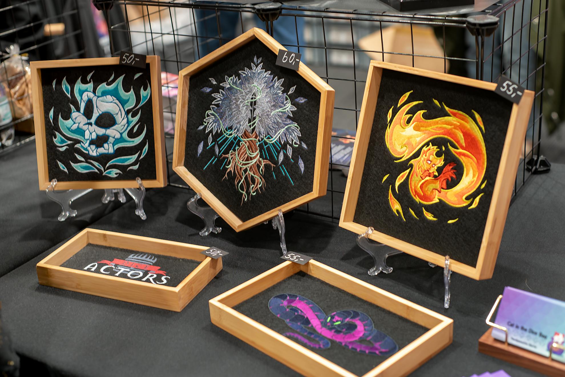 Eine Übersicht der Dice Trays: Gynther, Silberbaum, Fridolin, Dice-Actors-Logo und die Verhüllte Schlange auf dem Verkaufstisch der AnimagiC 2025.