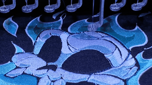 Nahaufname: Das Gynther-Motiv wird mit der Profi-Maschine auf den Stoff für Dice Trays gestickt.