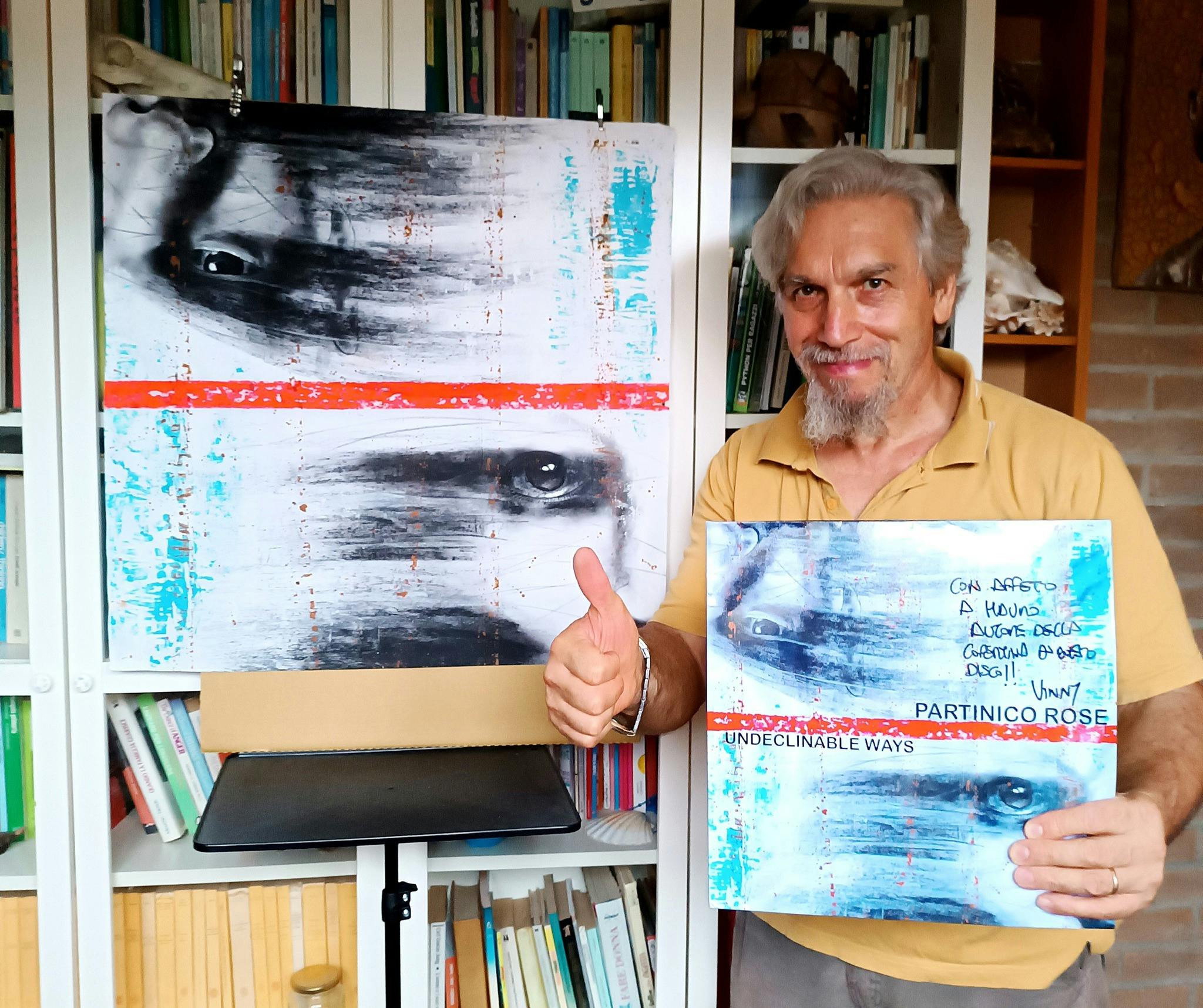 Artista con vinile e quadro coordinato, pollice in su davanti a una libreria.