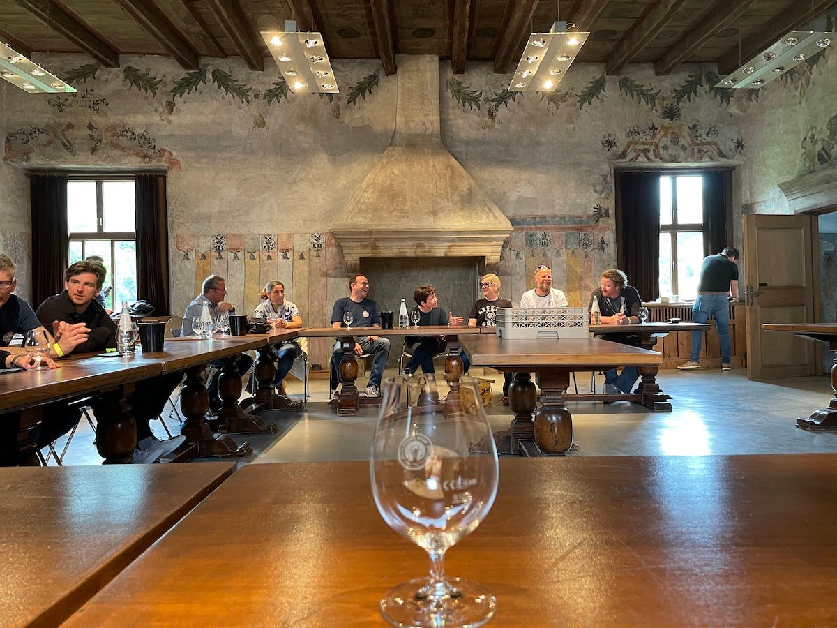 Masterclass im Schloßsaal. Leeres Glas im Vordergrund. Im Hintergrund Menschen an einem Hufeisenförmigen Tisch.
