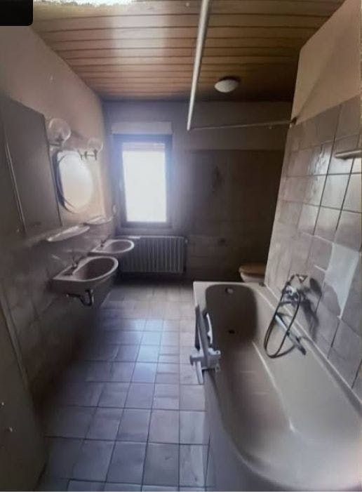Foto des Bades vor dem Umbau: Badewanne, zwei Waschbecken, Toillette, enge Durchgänge, insgesamt veraltet