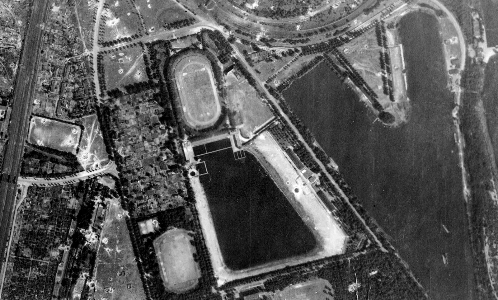 Schwarz-weiß Luftbild von der Sportanlage Wedau in Duisburg, aus den 1940er Jahren. Zu sehen sind das ovale alte Wedaustadion, ein Fußballplatz, ein Schwimmbad und die Regattabahn.