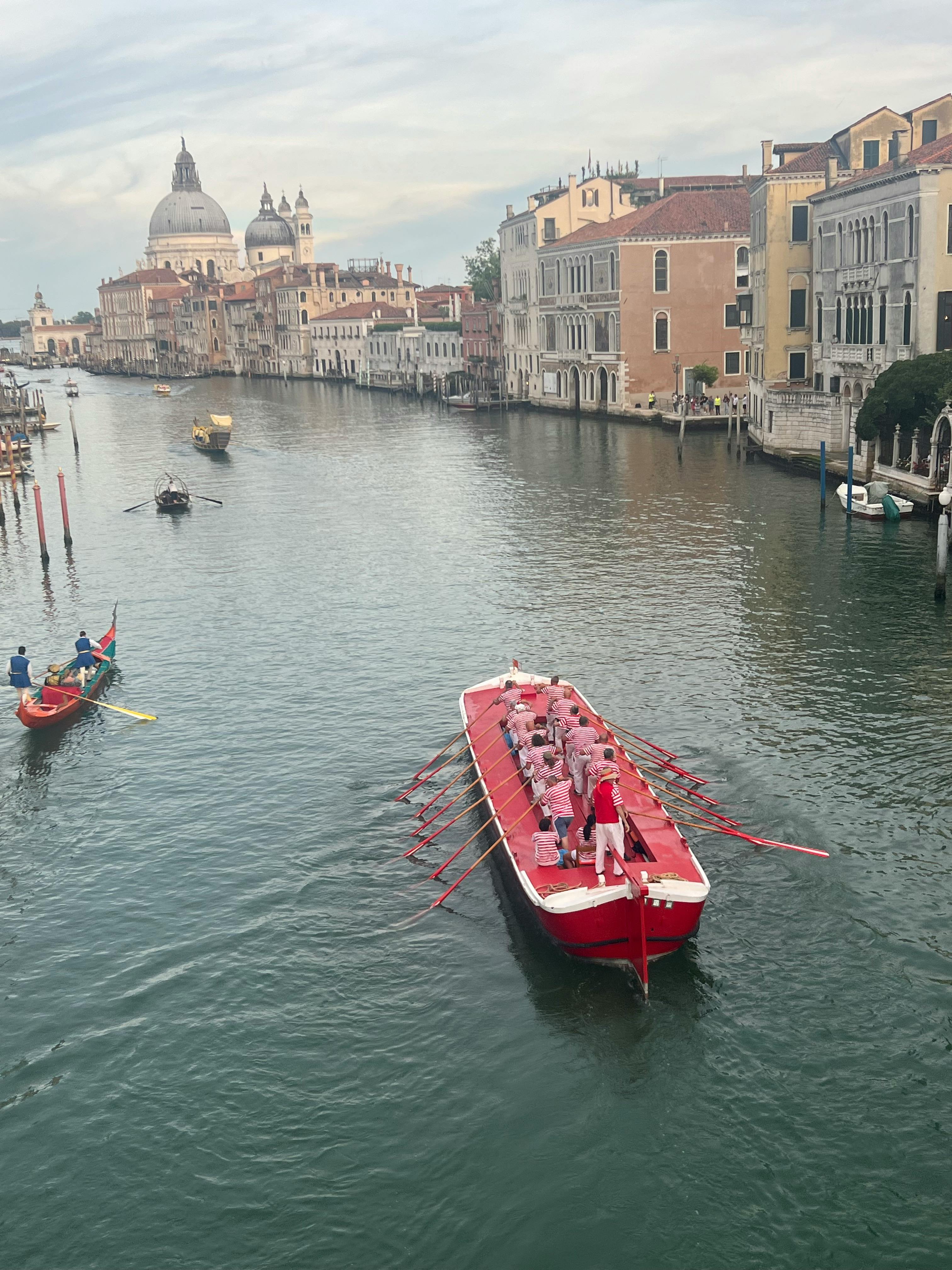 Foto von einem großen Ruderboot auf dem Canal Grande, das nach der Regata Storica zurückfährt. Im Hintergrund die Salute-Kirche.