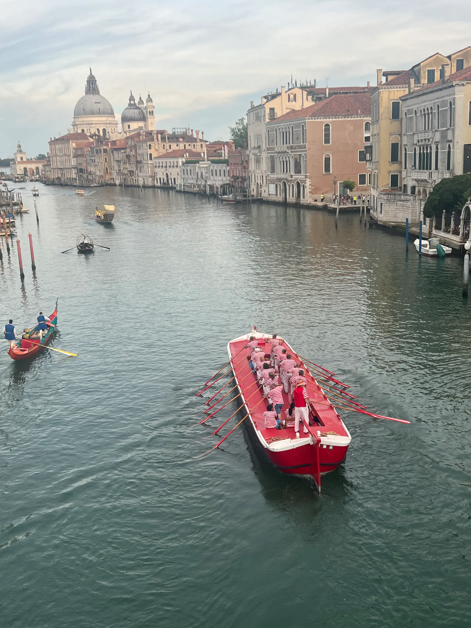 Foto von einem großen Ruderboot auf dem Canal Grande, das nach der Regata Storica zurückfährt. Im Hintergrund die Salute-Kirche.