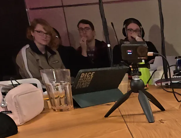 Die Aufnahme einer seitlichen Battlecam zeigt Stephie, Aylin, Philipp und Carina in der Technikecke; alle sehen angespannt und bestürzt in die Richtung, in der Rieke sitzt.