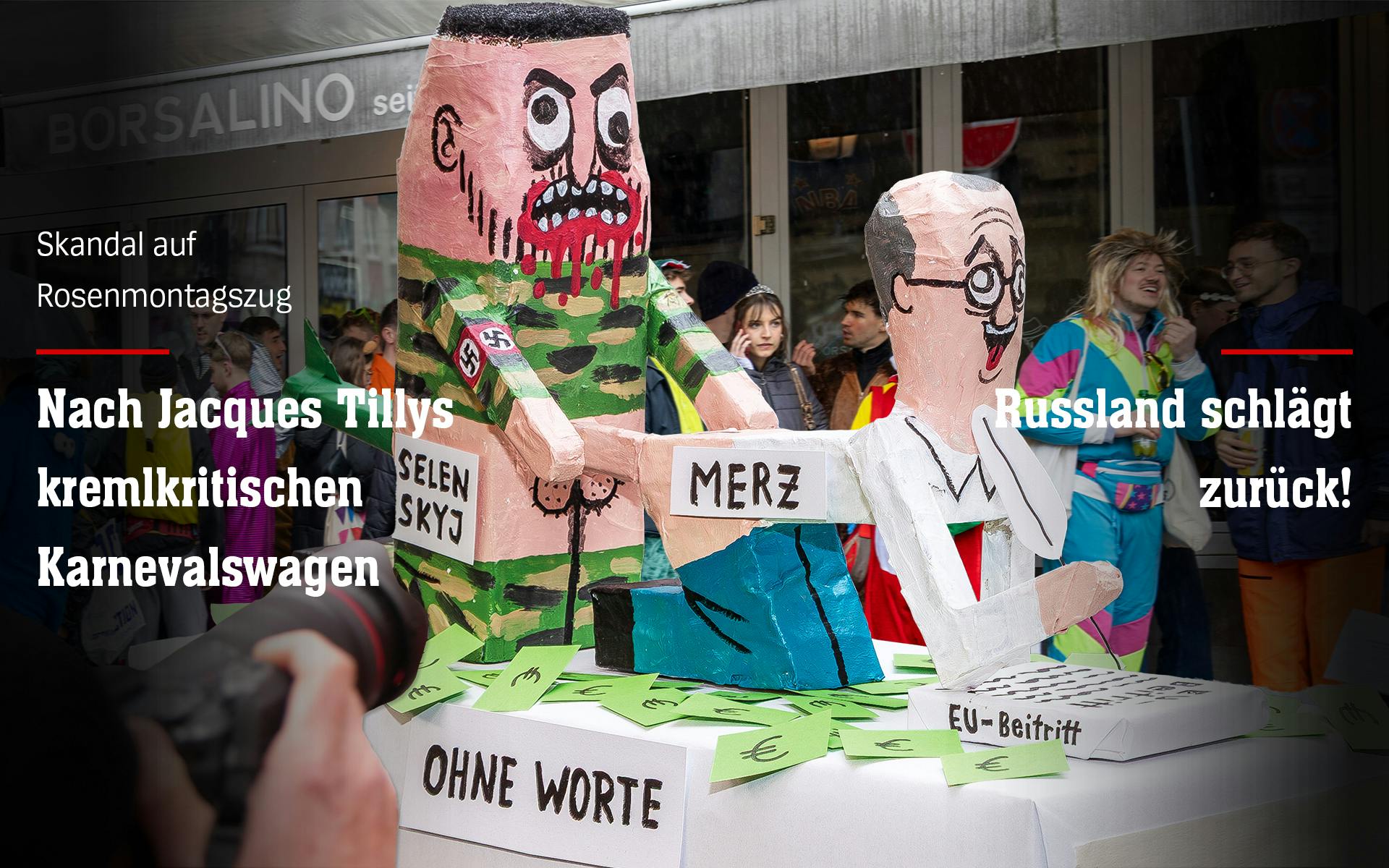 Fotomontage: zwei Pappmascheefiguren auf einem Karnevalswagen, im Hintergrund verkleidete Umzugsbesucher*innen. Die beiden Pappmascheefiguren stellen Selenskyj und Merz dar: Merz kniet mit heruntergelassener Hose und begeistertem Gesichtsausdruck vor Selenskyj und unterschreibt einen EU-Beitrittsvertrag, während er anal von Selenskyj penetriert wird. Selenskyjs Gesicht ist blutverschmiert, er hat die Zähne gefletscht und trägt eine Hakenkreuzbinde am rechten Arm. In seinem Rektum steckt eine Rakete. Die beiden knien auf über den Boden verteilten Euroscheinen. Auf Selenskyj steht "Selenskyj", auf Merz "Merz", vor den beiden ein Schild mit der Aufschrift "Ohne Worte". Über dem Foto steht der Text: "Skandal auf Rosenmontagszug: Nach Jaques Tillys kremlkritischen Karnevalswagen - Russland schlägt zurück!"