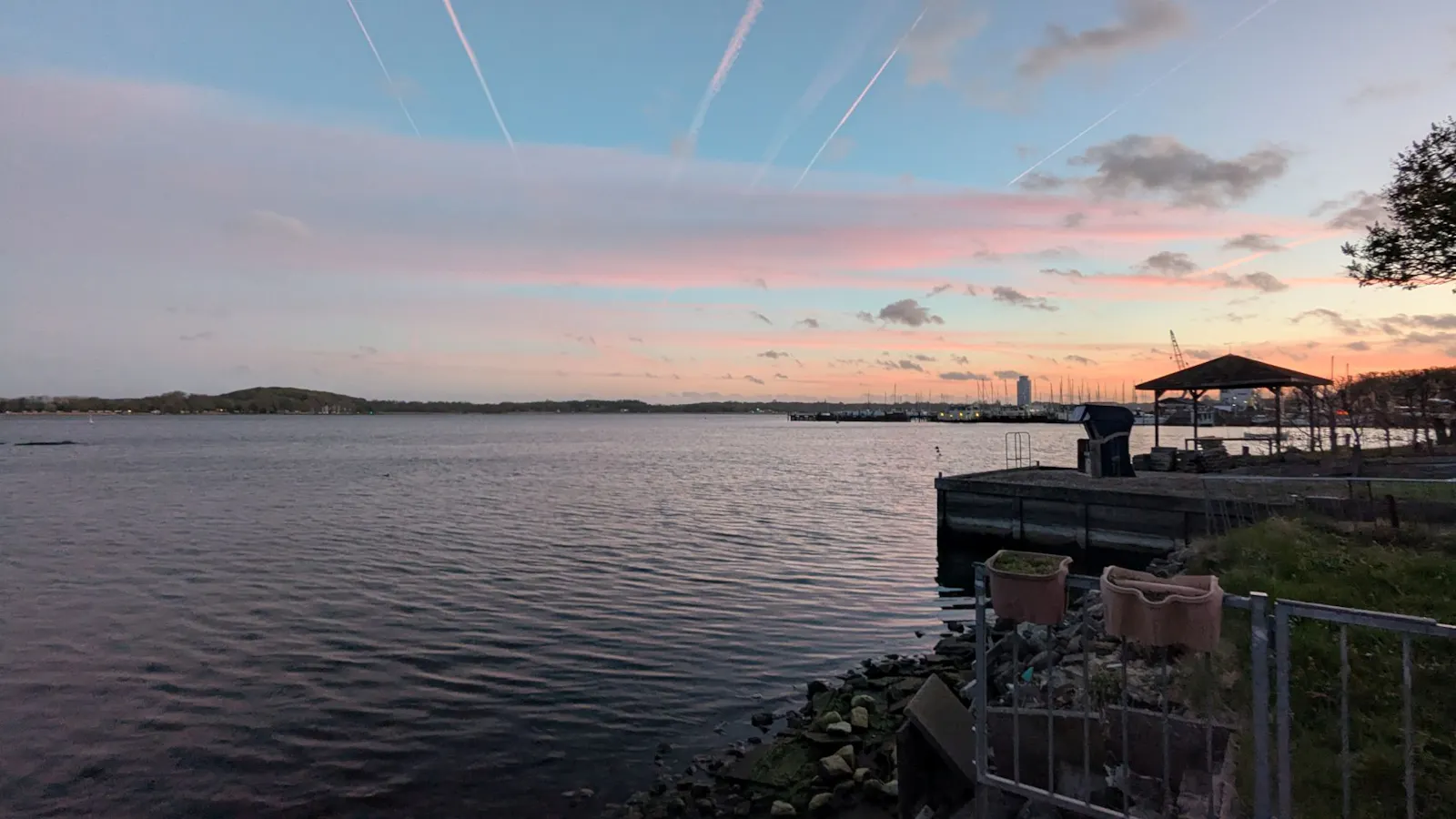 Ein Blick über die Schlei bei Schleswig in der Abenddämmerung. Die Wolken werden von der untergehenden Sonne rötlich gefärbt. Am Horizont jenseits des Wassers ist der Hügel zu erkennen, in dessen Nähe sich die alte Wikingersiedlung Haithabu befindet.