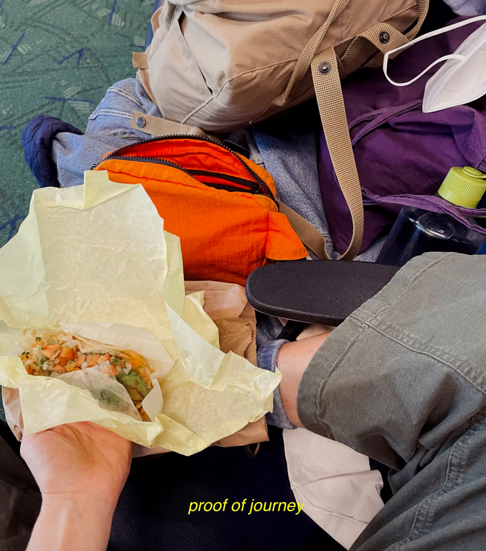 Von oben nach unten: Ein Rucksack, eine FFP2-Maske, eine Bauchtasche, ein Stoffbeutel, all das auf einer Jeansjacke, eine Wasserflasche, links Svenjas Hand und darin ein Taco. Unten steht in gelber Schrift "proof of journey"