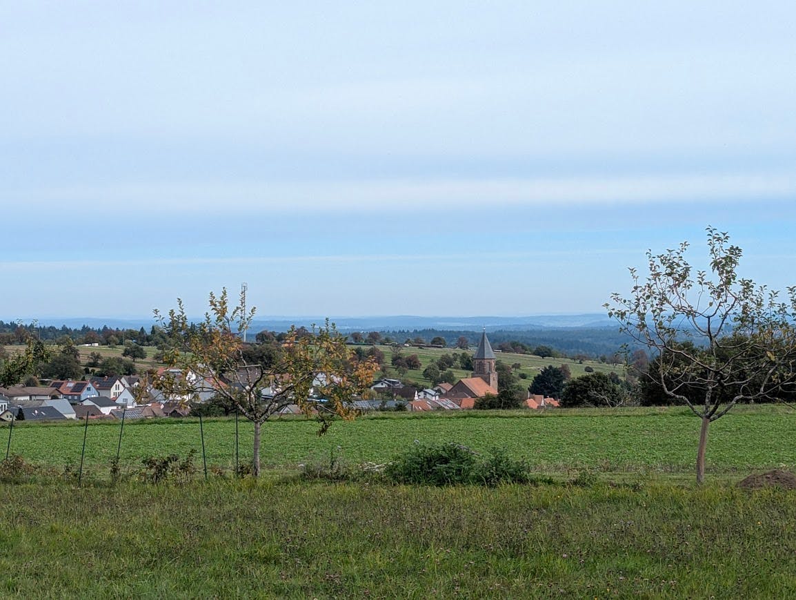 Fernblick mit Dorf samt Kirche im Vordergrund bis zu einer weit entfernten Hügellinie