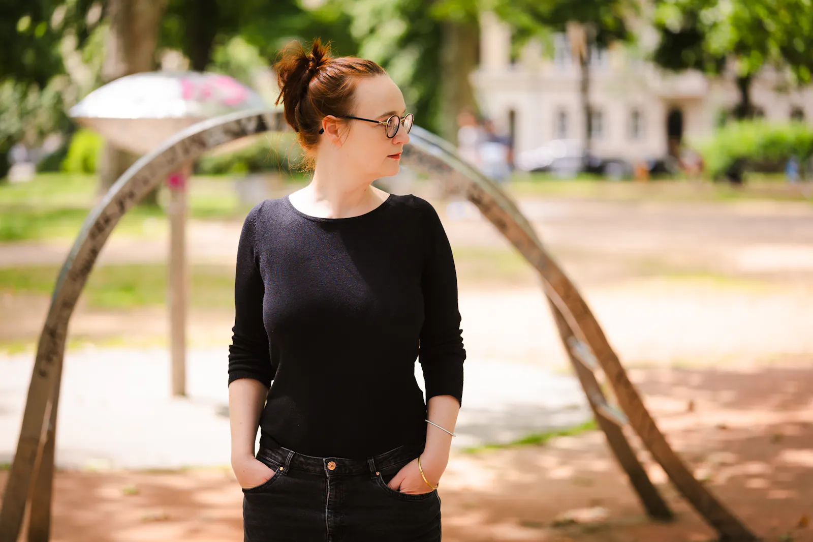 Insa van den Berg, Frau mit roten Haaren und Brille, steht auf Spielplatz, schaut zur Seite.