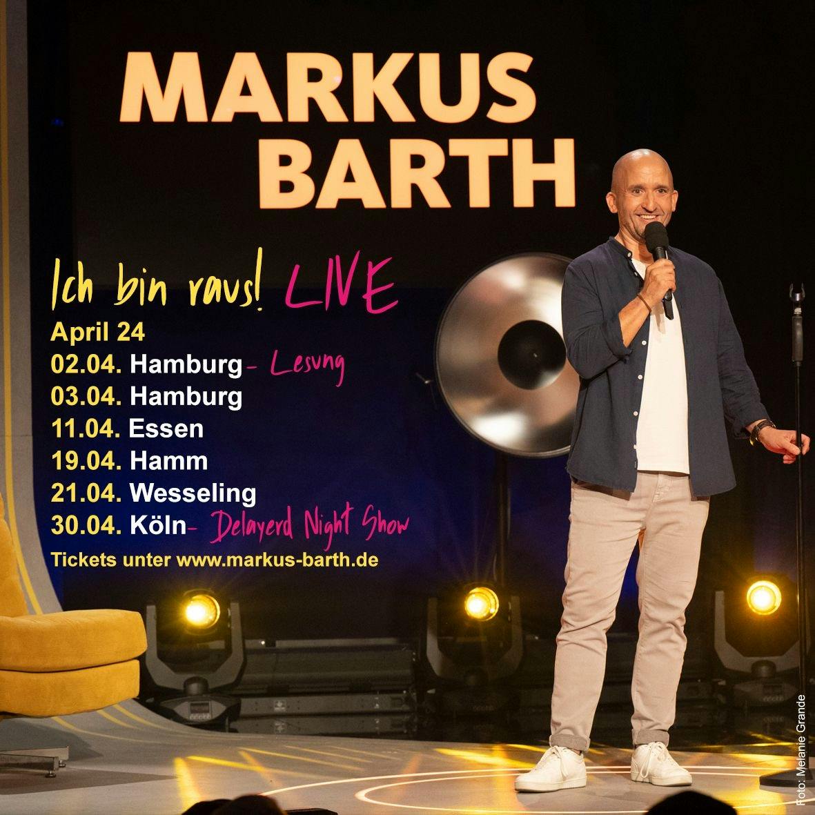 Ich stehe auf einer Bühne, habe ein Mikro in der Hand und halte mich am Stativ fest. Daneben stehen Termine meiner Live Tour.