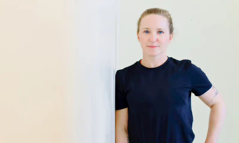 Nici in schwarzem T-Shirt an die Wand gelehnt, lächelnd