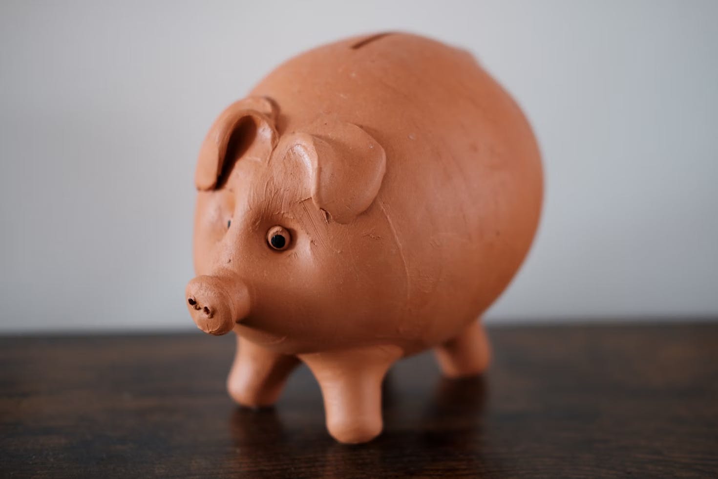 Selbstgetöpfertes, rosa Sparschwein auf einem braunen Tisch.