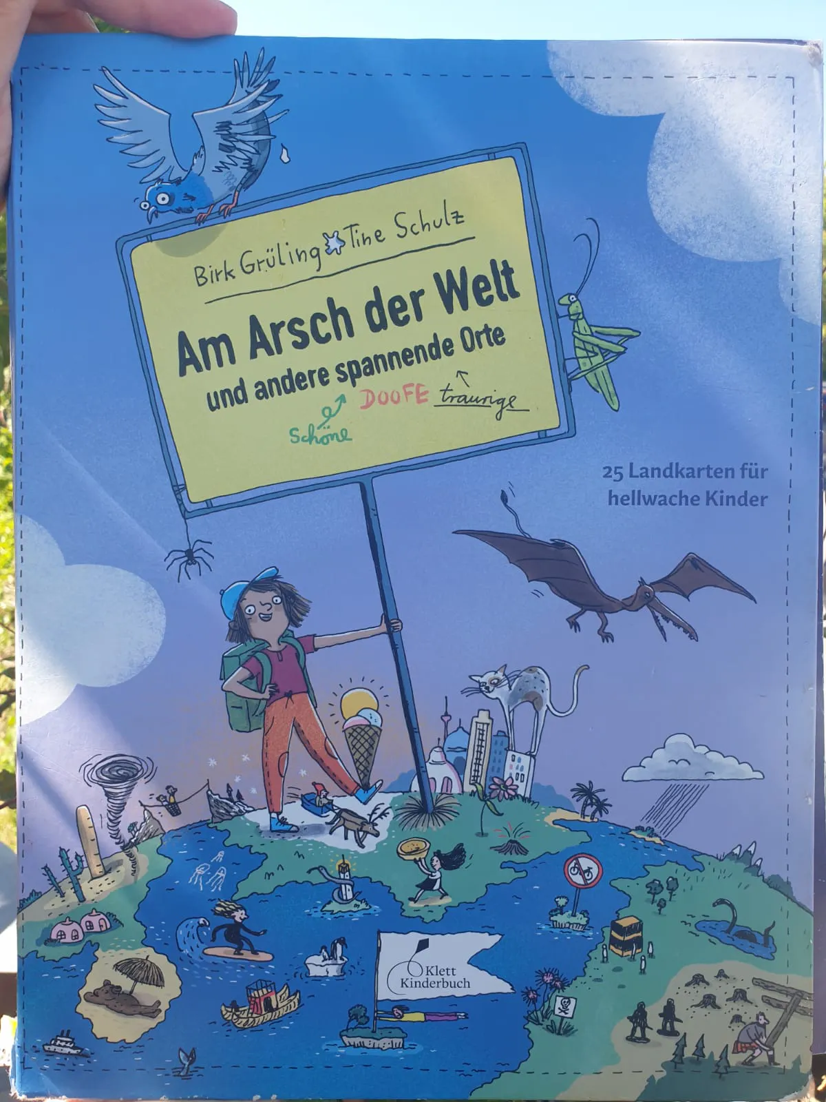 Cover des Bilderbuches "Am Arsch der Welt und andere spannende Orte". Klett Verlag. Zu sehen ist ein Stück einer blauen Weltkugel, auf der ein Mädchen mit Rucksack steht und sich an einem Schild festhält. Die Beschriftung des Schildes stellt den Buchtitel dar.