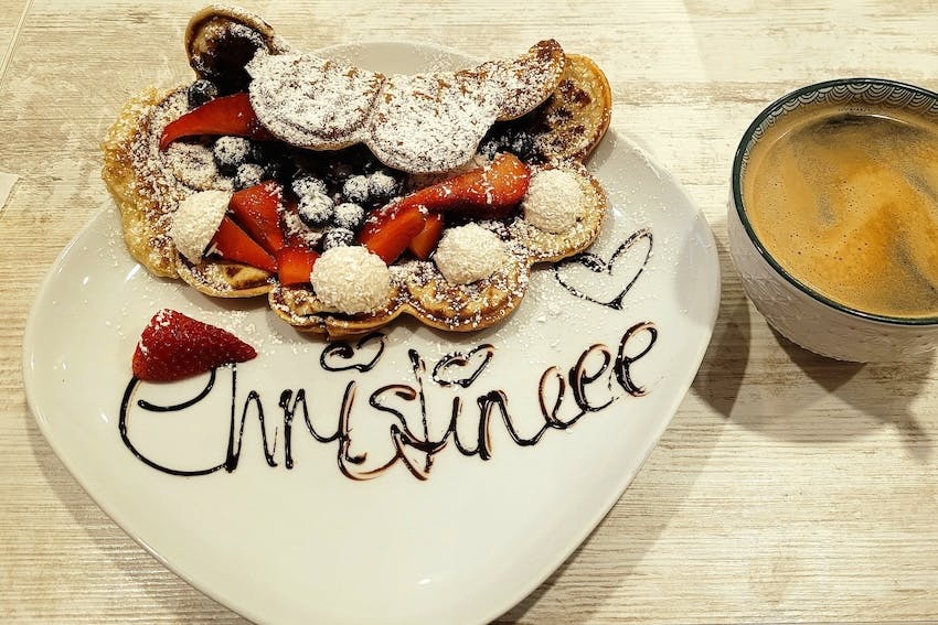 Waffel mit Obst und Kokosraspeln auf einem Teller, auf dem mit Schokoladensauce der Name Christine geschrieben ist