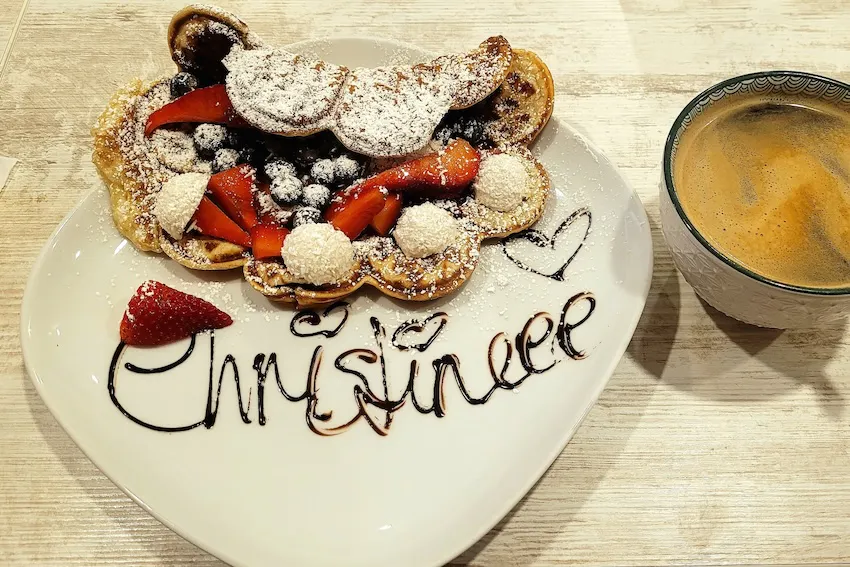 Waffel mit Obst und Kokosraspeln auf einem Teller, auf dem mit Schokoladensauce der Name Christine geschrieben ist