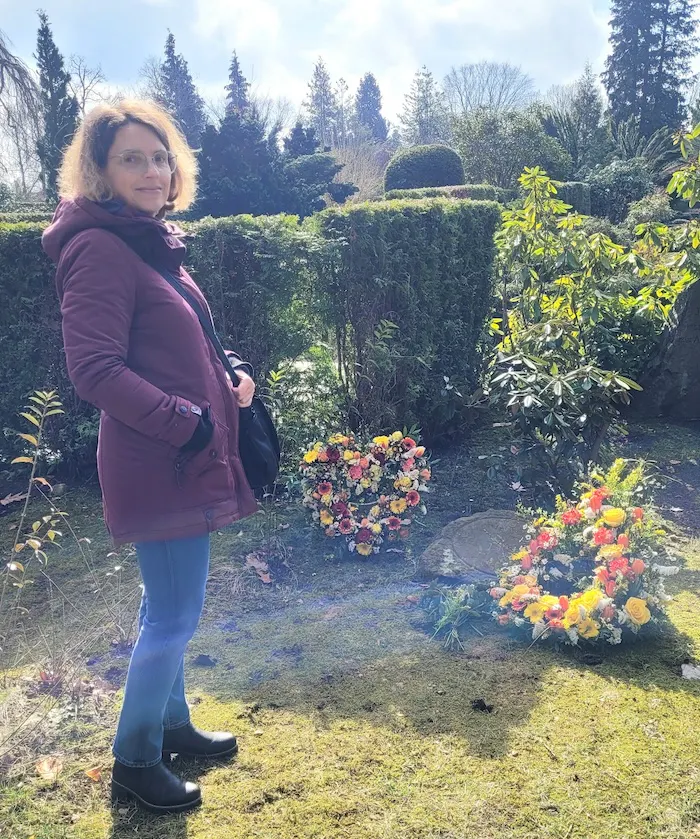 Christine Piontek bei Sonnenschein auf dem Friedhof an einem mit Blumen geschmückten Grab