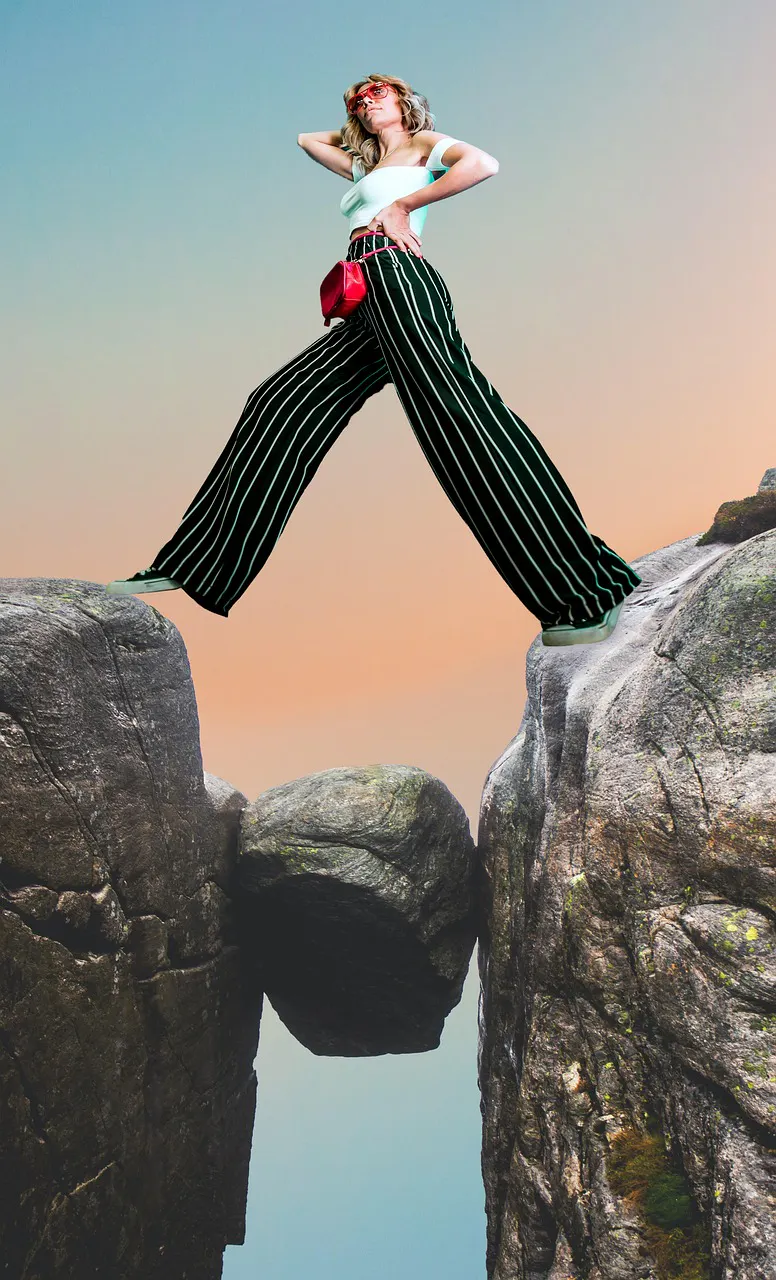 eine Frau die sicher über einem Abgrund zwischen zwei Felsen steht, je mit einem Bein auf einer Seite.