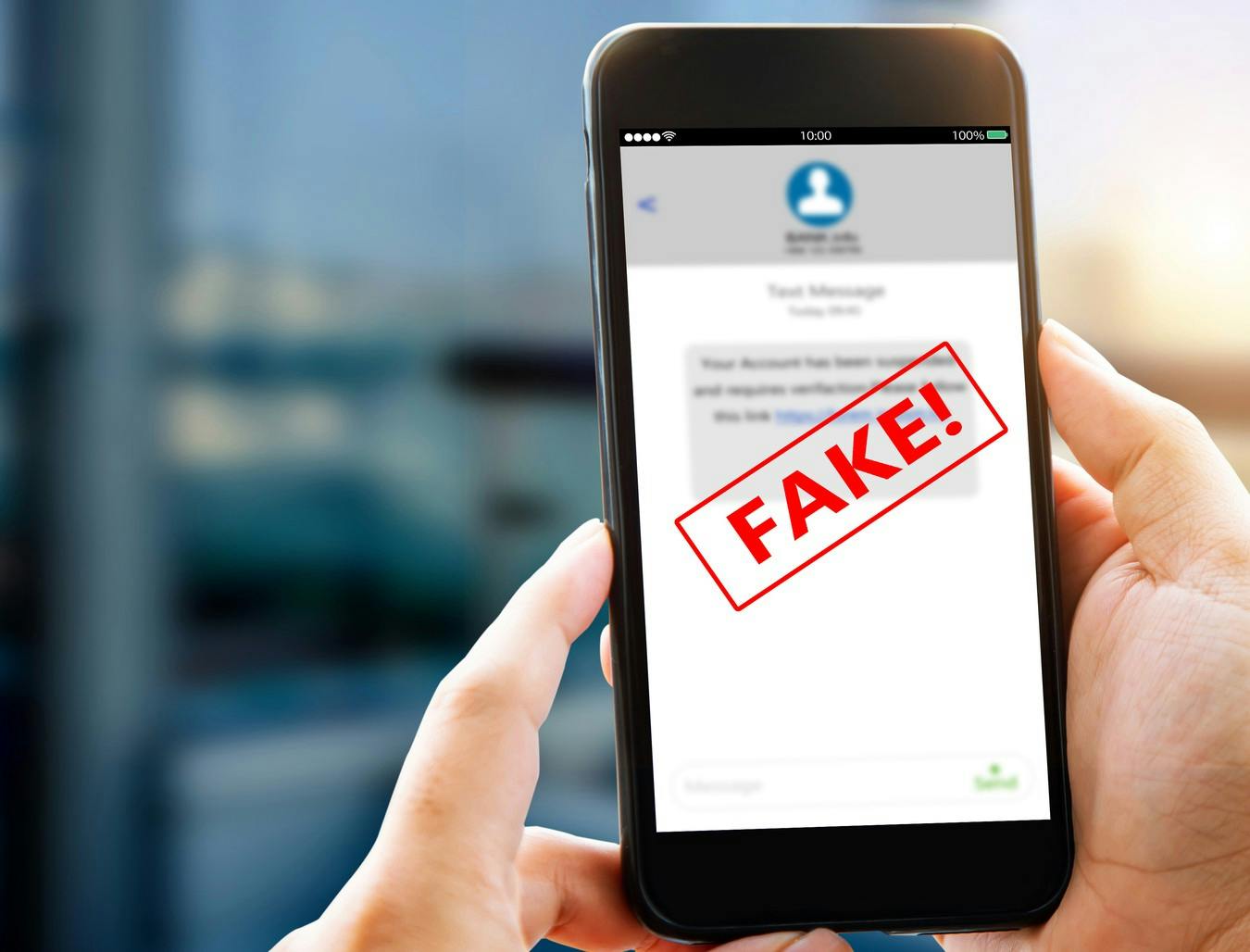 Dieses Foto zeigt eine Person, die ein Smartphone in der Hand hält, auf dessen Bildschirm eine SMS-Nachricht zu sehen ist, über die groß und rot das Wort „FAKE!“ eingeblendet ist.