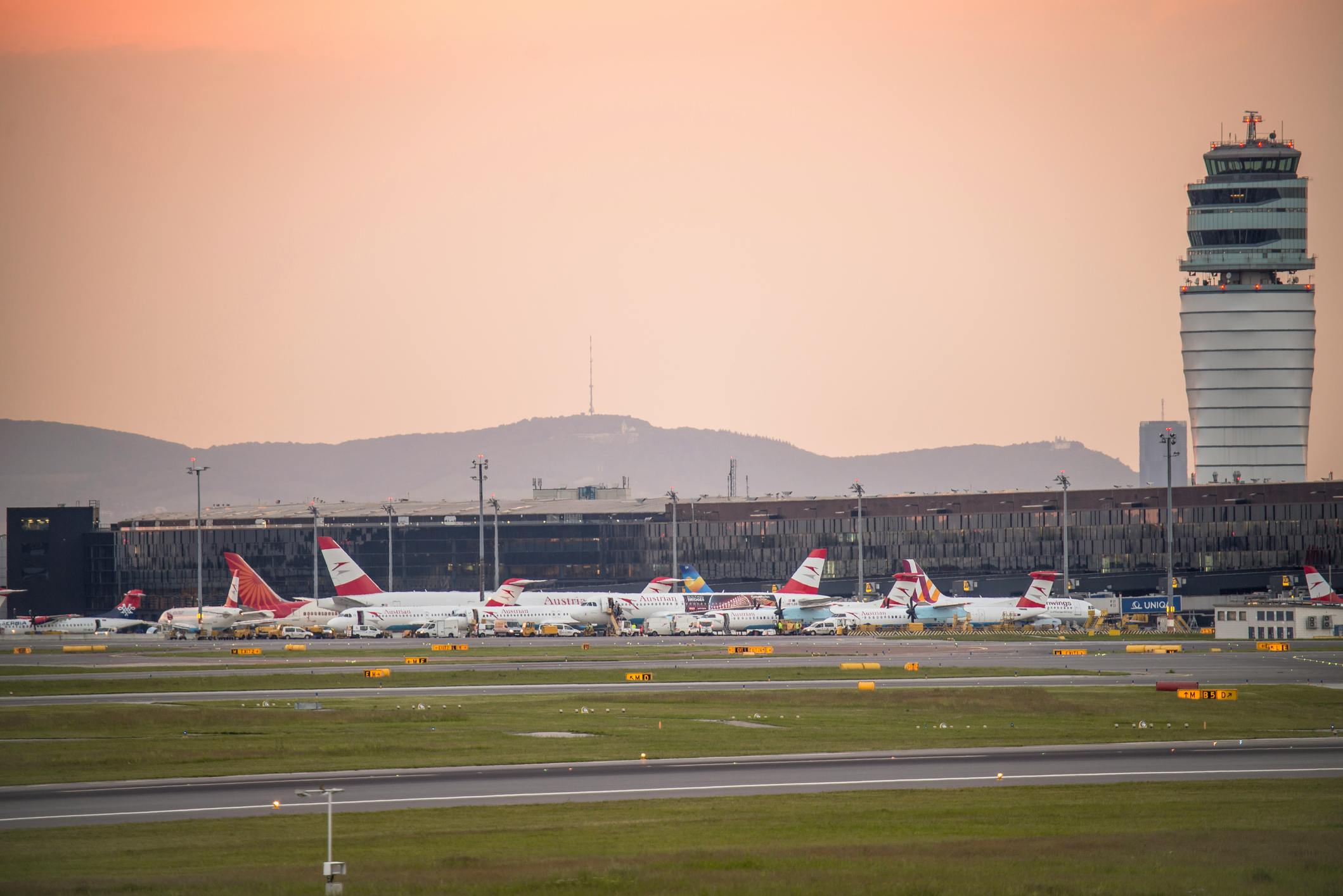 Das Foto zeigt den Flughafen Wien-Schwechat mit mehreren Flugzeugen, Terminals und dem Tower.