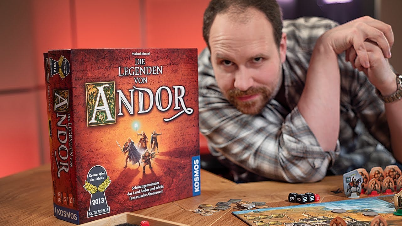 Alex blickt frech in die Kamera. Vor ihm steht präsent die Spielverpackung von "Die Legenden von Andor".