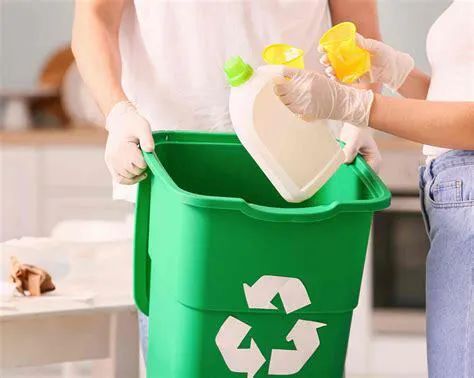 Menschen in weißen T-Shirts füllen Plastikmüll in eine grüne Recycling Mülltonne.