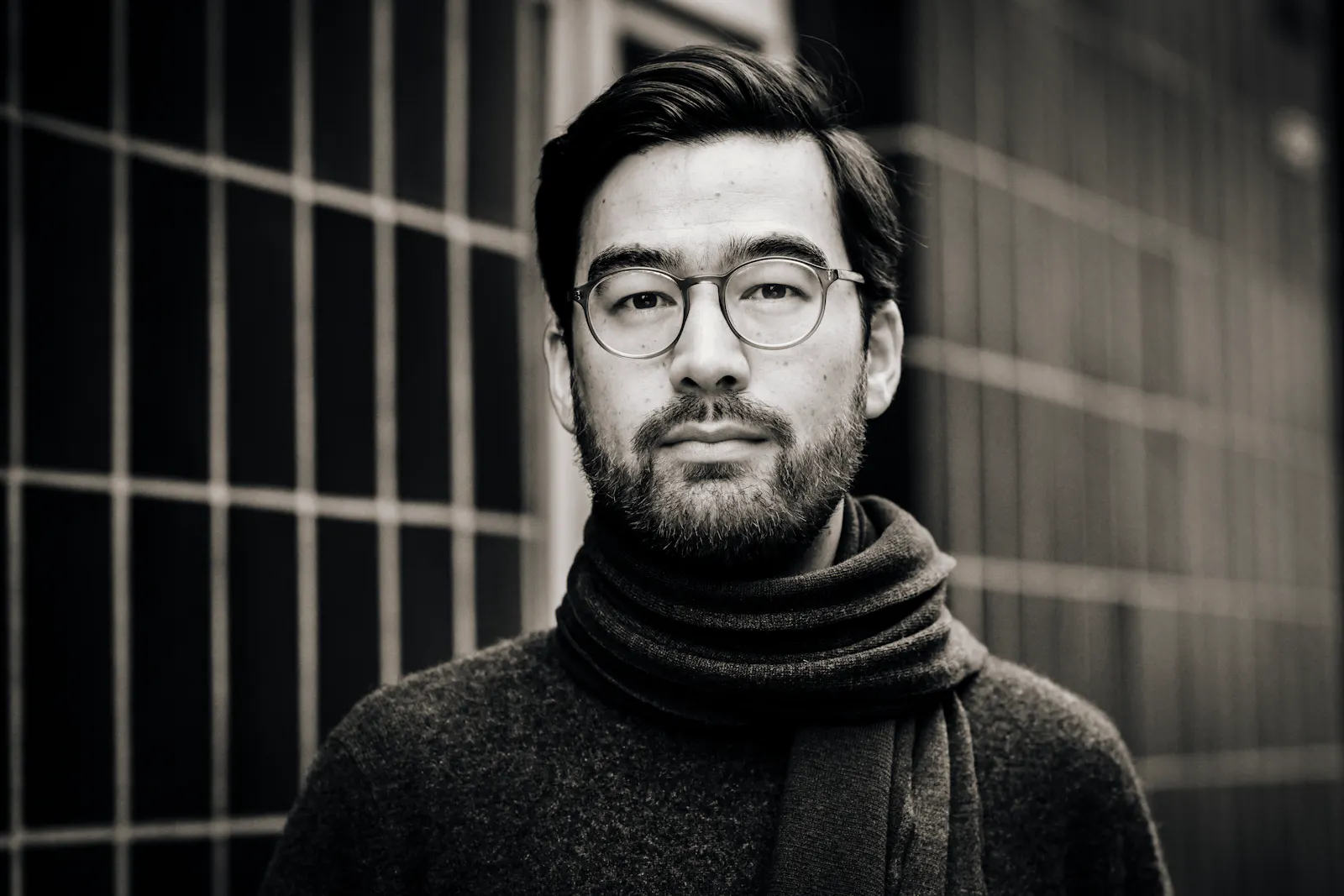 Yannic Han Biao Federer trägt einen dunklen Wollpullover und einen Schal. Er schaut ernst in die Kamera, hinter ihm ist ein Gitter zu sehen. Das Bild ist in Schwarz-Weiß.