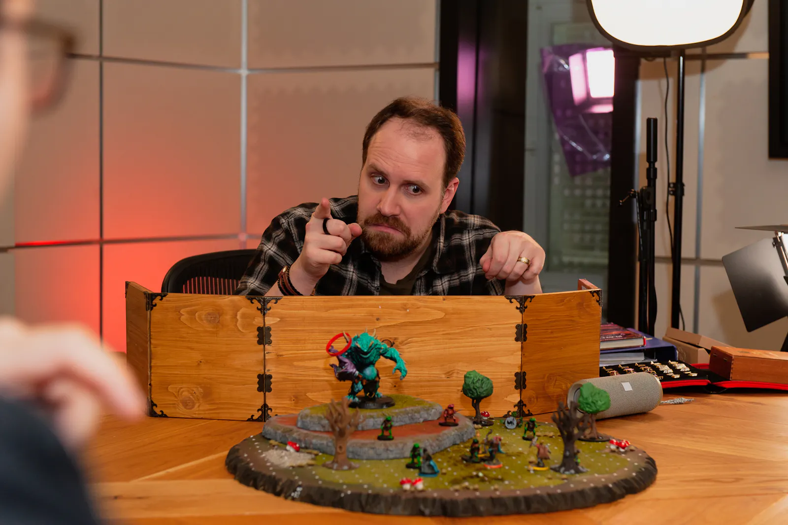 Alex guckt ernst auf eine Battlemap, auf der ein großer Gegner aufgebaut ist. Dabei zeigt er mit dem Finger in Richtung Spielis.
