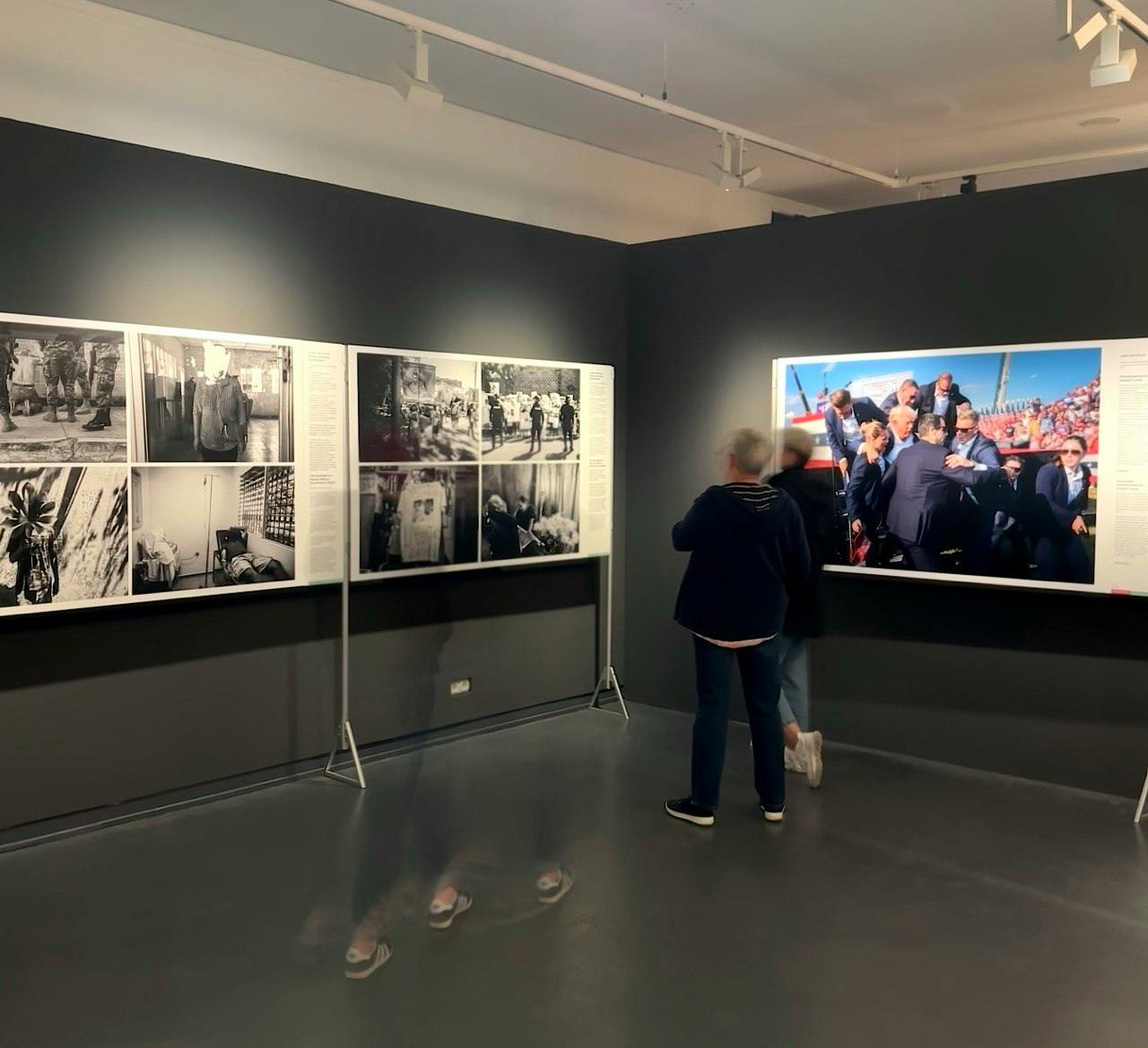 Foto aus der Ausstellung: Zwei Stellwände voller Fotos, davor verschwommen Personen.