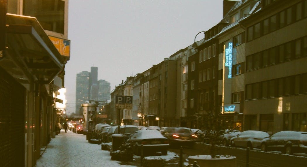 Eine Straße in Köln, es liegt etwas Schnee auf dem Bürgersteig, es ist neblig, im Hintergrund ist ein Hochhaus zu sehen.