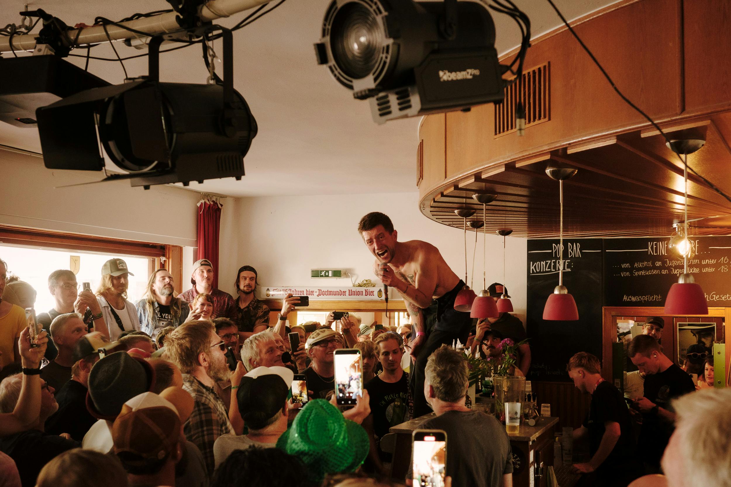 Die Band Heavy Lungs tritt in einer kleinen Bar beim Haldern Pop Festival auf, der Sänger steht auf der Theke, umringt von einem dicht gedrängten Publikum.