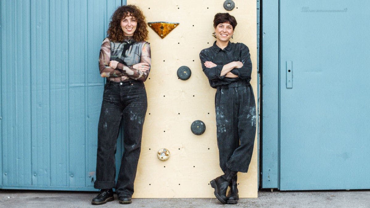 Marta und Manuela vom Startup "MAD" entwickeln Klettergriffe aus Pilzmyzel. Hier stehen sie vor einer Wand mit ihren Griffen.