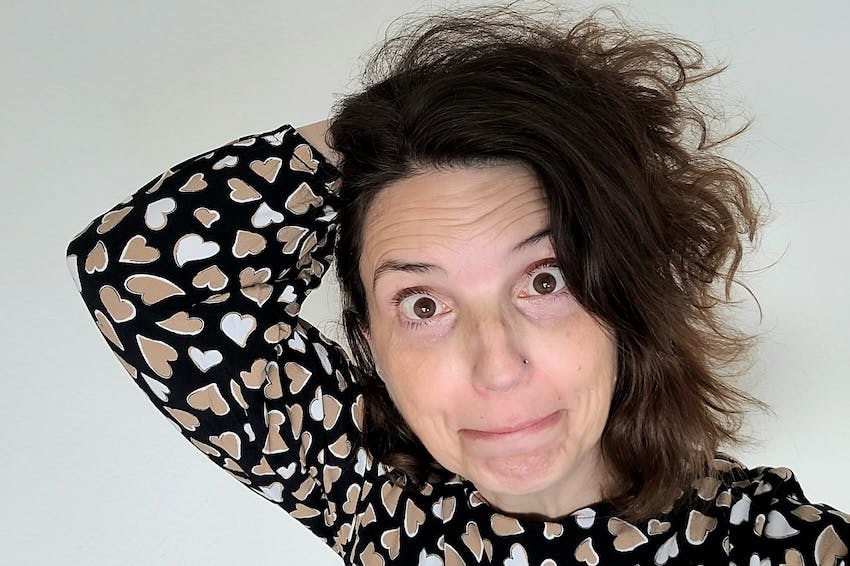 Christine Piontek im schwarzen Oberteil mit weißen und beigen Herzen schaut erstaunt und fährt sich durch die Haare.