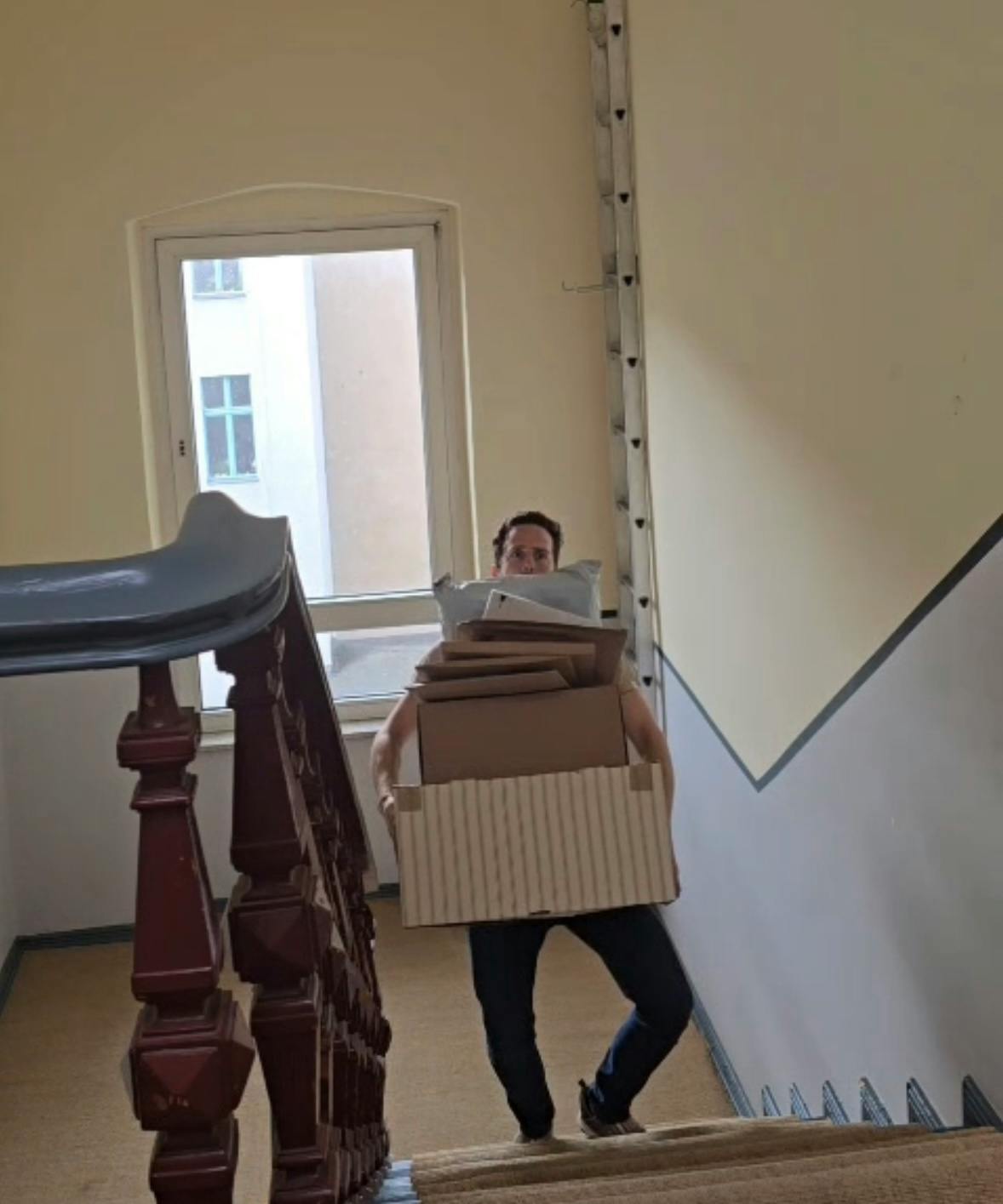 Ein Mann geht mit einem Stapel Pakete die Treppe hoch