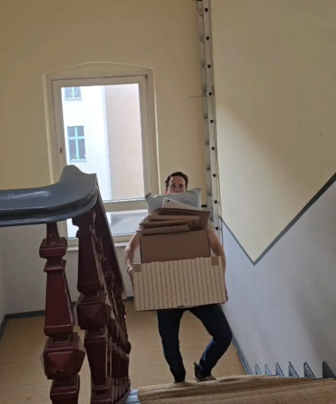 Ein Mann geht mit einem Stapel Pakete die Treppe hoch