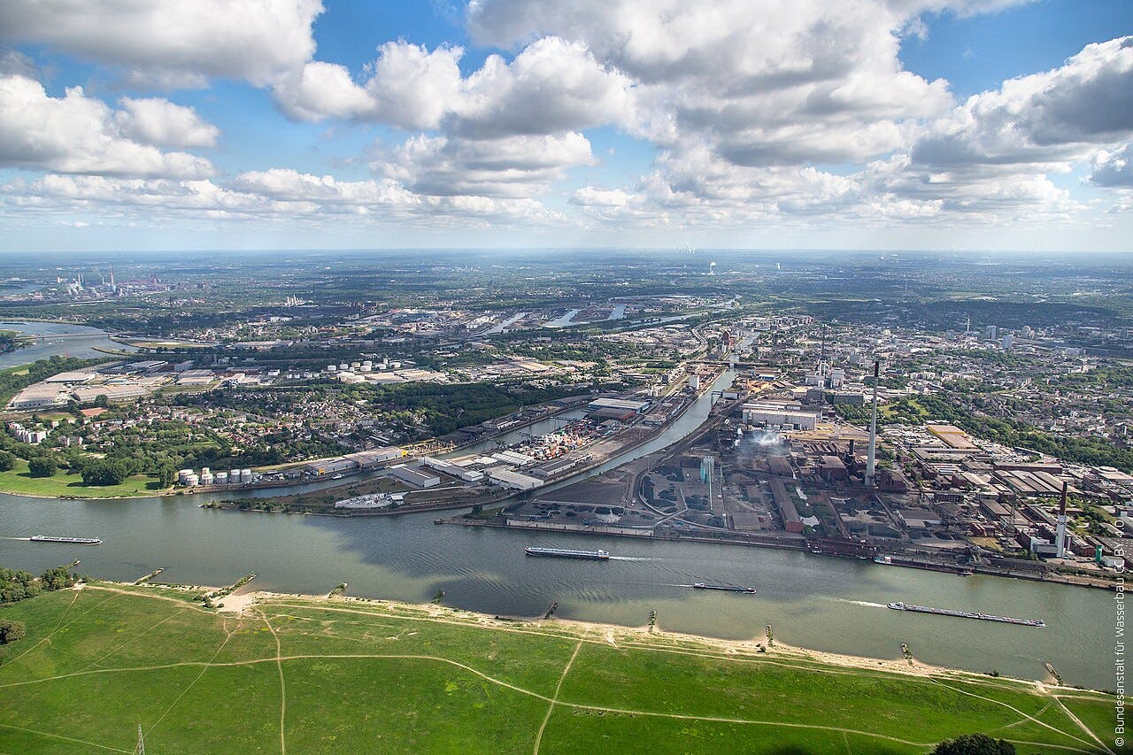 Luftbild von Duisburg im Vordergrund der Rhein und darüber Schäfchenwolken. Es ist Sommer.