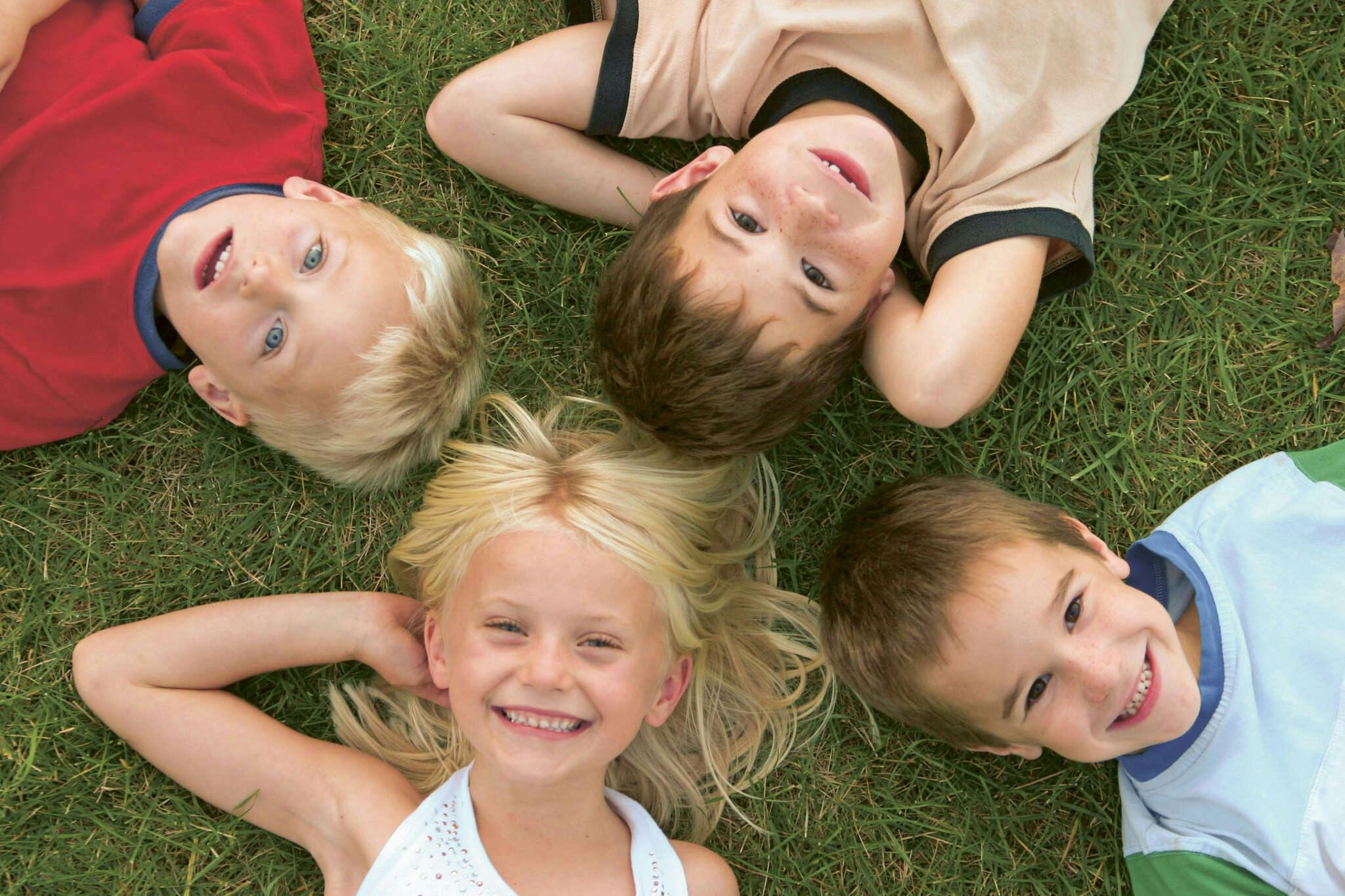 4 Kinder, 3 Jungs und ein Mädchen, liegen auf dem Gras. Die Köpfe bilden einen Stern, die Kinder lachen.