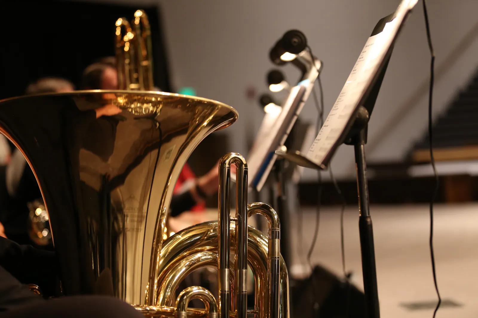 Gold glänzende Tuba, beleuchtete Notenpulte, im Hintergrund Musizierende