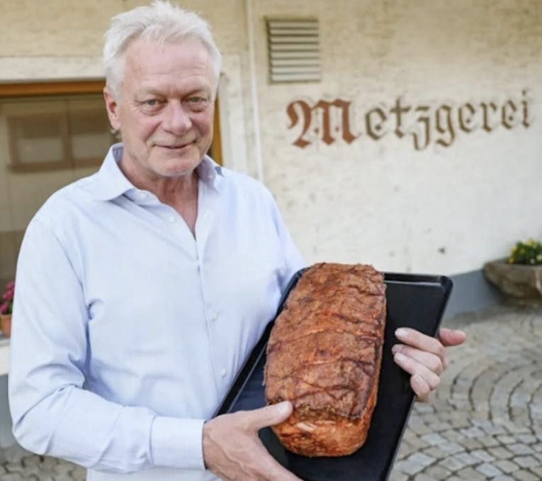 Alois Rainer vor seiner Metzgerei, einen Leberkäs präsentierend