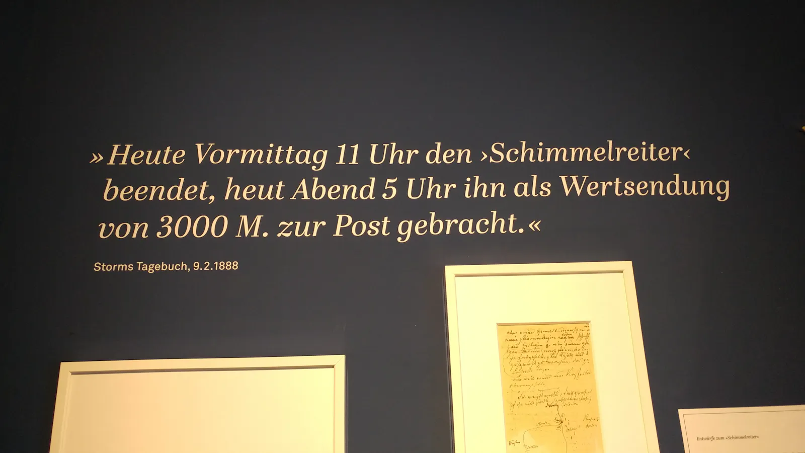 Eine Wand mit dem Spruch: "Heute Vormittag 11 Uhr den 'Schimmelreiter' beendet, heut Abend 5 Uhr ihn als Wertsendung von 3000 M. zur Post gebracht."
Storms Tagebuch 9.2.1888